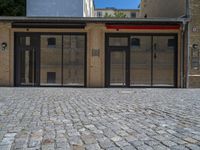 the sidewalk is paved with stones and has a bench in front of it, with no people inside