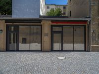 the sidewalk is paved with stones and has a bench in front of it, with no people inside