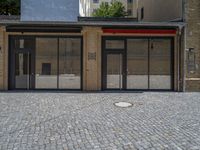 the sidewalk is paved with stones and has a bench in front of it, with no people inside