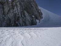 a person is skiing in the snow on a steep hill with a huge rock formation in the back