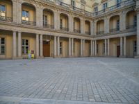 a courtyard with a building on the other side and a large white building with many windows