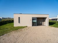 a gravel road with a small building in front of it in a grassy area on the other side is the house