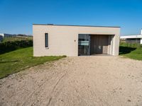 a gravel road with a small building in front of it in a grassy area on the other side is the house