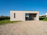 a gravel road with a small building in front of it in a grassy area on the other side is the house