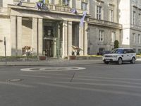 an image of a white car driving down the road on a road corner in front of a large building