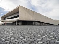 a small child walking towards a large building with a ramp on top of it on a cobblestone street