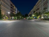 an empty street at night with the light turned on and cars parked on it in the distance