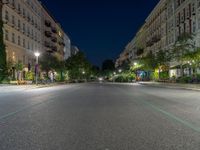 an empty street at night with the light turned on and cars parked on it in the distance