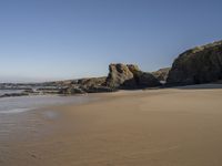 an empty beach with sand and rocks in the background with clear blue skies and water