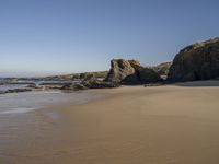 an empty beach with sand and rocks in the background with clear blue skies and water