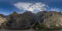 view of mountains with small clouds on top of them and water at bottom of mountain