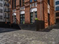 a sidewalk with chairs next to the brick building on the side, some have stairs and some buildings in the background