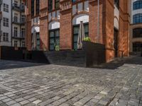 a sidewalk with chairs next to the brick building on the side, some have stairs and some buildings in the background