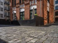 a sidewalk with chairs next to the brick building on the side, some have stairs and some buildings in the background