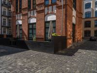 a sidewalk with chairs next to the brick building on the side, some have stairs and some buildings in the background