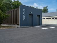 a metal building with a corrugated door in front of it and trees lining the street behind it