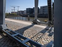 the bridge has an old metal bench beside the side of it and buildings along the river bank