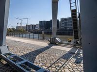 the bridge has an old metal bench beside the side of it and buildings along the river bank