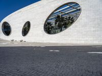 a street in front of a white building with two circular windows on the wall, as if in the street,