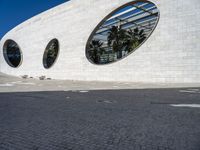 a street in front of a white building with two circular windows on the wall, as if in the street,
