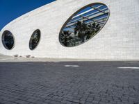 a street in front of a white building with two circular windows on the wall, as if in the street,