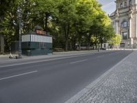 there is a street with trees along side and a building across it from them on the right