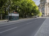 there is a street with trees along side and a building across it from them on the right