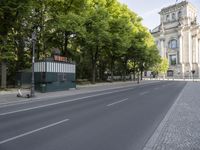 there is a street with trees along side and a building across it from them on the right