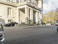 cars driving down a city street near the large building with the blue flag flying in front