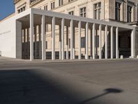 white building with columns at the entrance and people standing on the sidewalk outside it,