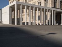 white building with columns at the entrance and people standing on the sidewalk outside it,