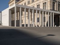 white building with columns at the entrance and people standing on the sidewalk outside it,