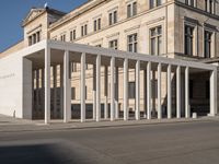 white building with columns at the entrance and people standing on the sidewalk outside it,