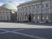 the european building features a paved stone courtyard and several old style cars parked in front