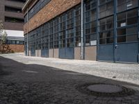 an old brick building with many windows and small door panels on it, in front of an empty courtyard