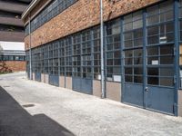 an old brick building with many windows and small door panels on it, in front of an empty courtyard