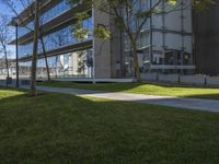 a paved path with trees along the grass next to a building and two buildings in the distance