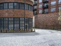 a brick circular building with windows and two benches in front of it on a brick pavemented area