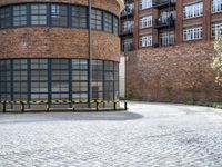 a brick circular building with windows and two benches in front of it on a brick pavemented area