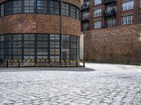 a brick circular building with windows and two benches in front of it on a brick pavemented area