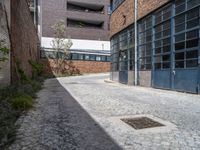 an empty brick building next to a small street with a door and a manhole