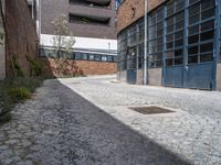 an empty brick building next to a small street with a door and a manhole