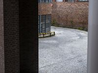 a bench sits in front of a red brick wall behind a metal pole in the middle of the courtyard