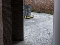 a bench sits in front of a red brick wall behind a metal pole in the middle of the courtyard