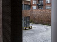 a bench sits in front of a red brick wall behind a metal pole in the middle of the courtyard