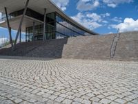 a person on a bike walking through a stone building entrance, in front of an enormous glass wall and stairs