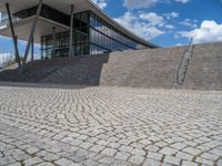 a person on a bike walking through a stone building entrance, in front of an enormous glass wall and stairs