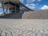 a person on a bike walking through a stone building entrance, in front of an enormous glass wall and stairs