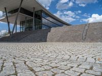 a person on a bike walking through a stone building entrance, in front of an enormous glass wall and stairs