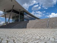 a person on a bike walking through a stone building entrance, in front of an enormous glass wall and stairs